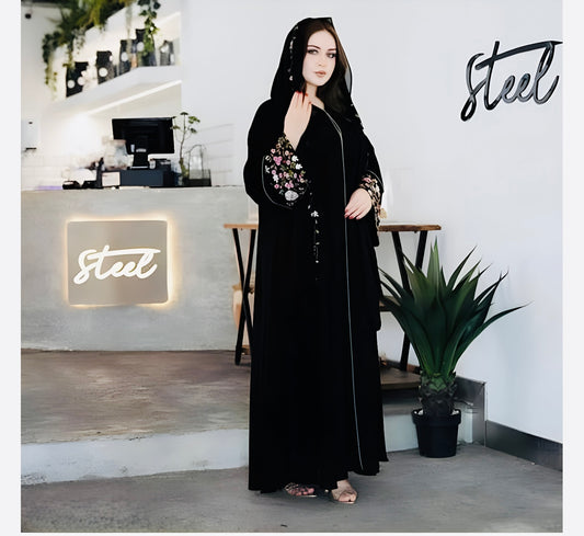 Woman wearing elegant premium abaya with floral embroidery in modern home setting showcasing modest yet stylish Islamic dress